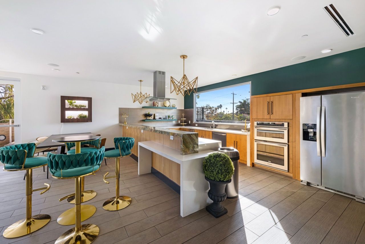 Bright open-concept kitchen with a large island, teal tufted stools, and stainless steel appliances.