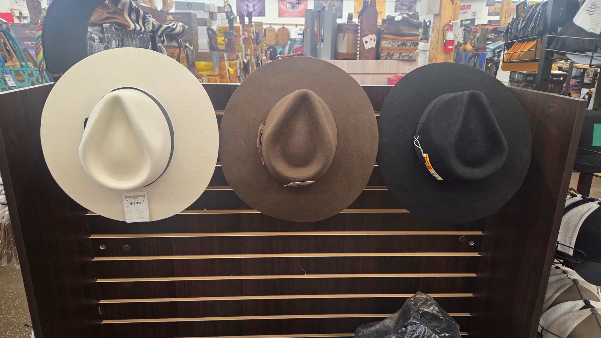 Three hats displayed on a rack: white, brown, and black.