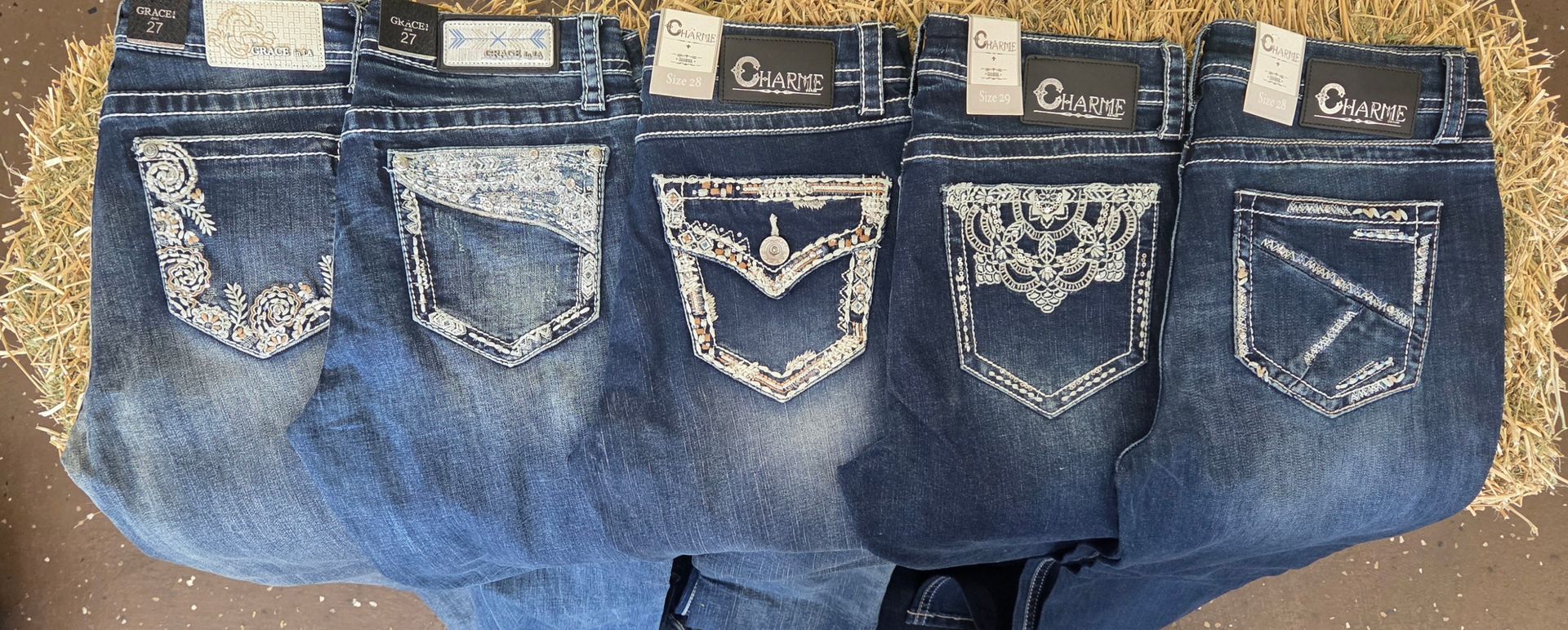 Five blue denim jeans laid out side by side, each with decorated back pockets and stitching details