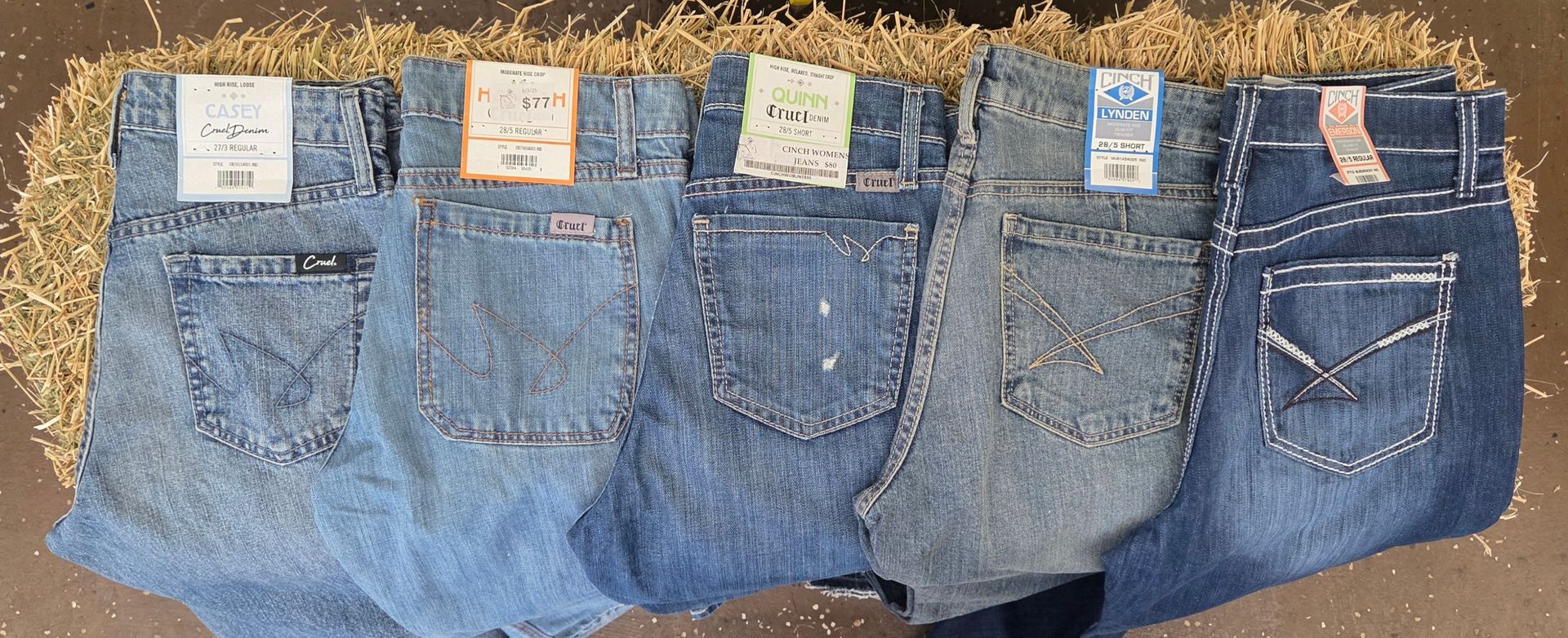 Five pairs of blue jeans laid side by side, showing back pockets and labels