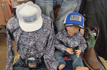 Two people in matching patterned shirts and patriotic hats sit side by side in a store.
