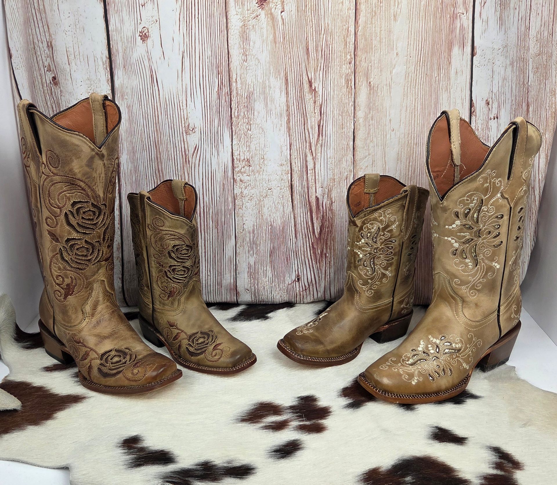 Four ornate cowboy boots arranged on a wooden floor before a rustic white backdrop.