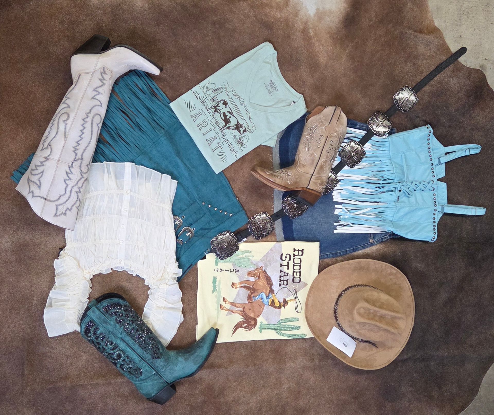 Scattered clothing and accessories on a carpet, including a blue dress, hat, boots, and a book.