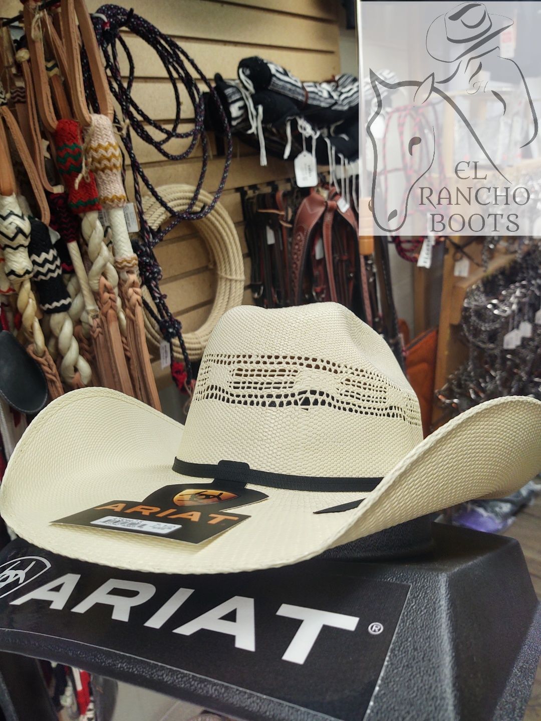 Straw cowboy hat on an Ariat box in a western boot shop, with saddles and bridles in the background