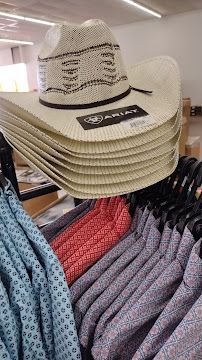 Stack of beige straw cowboy hats displayed above patterned shirts in a store.