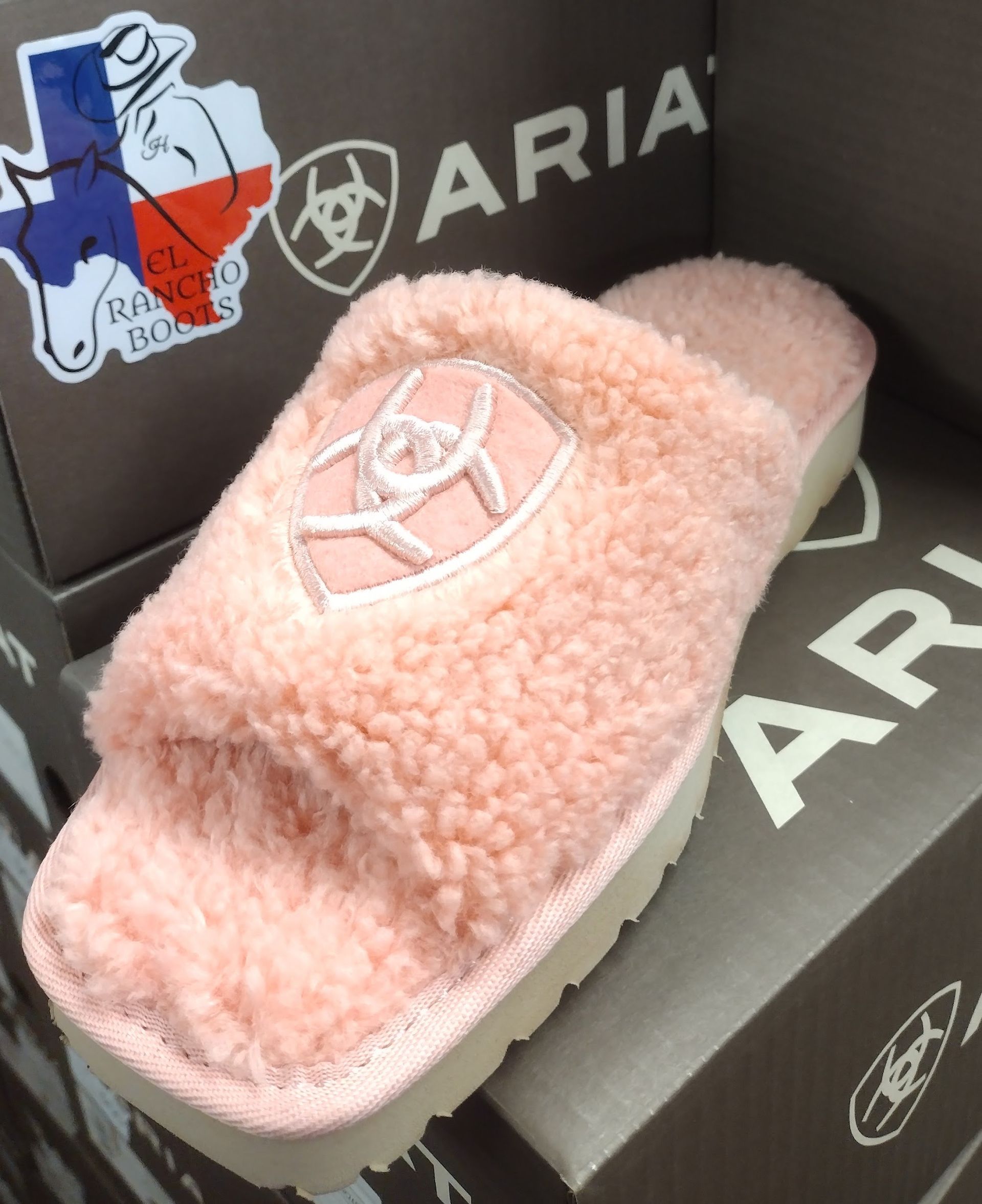 Pink fuzzy slide sandal on ARIA shoe boxes, with white sole and logo.