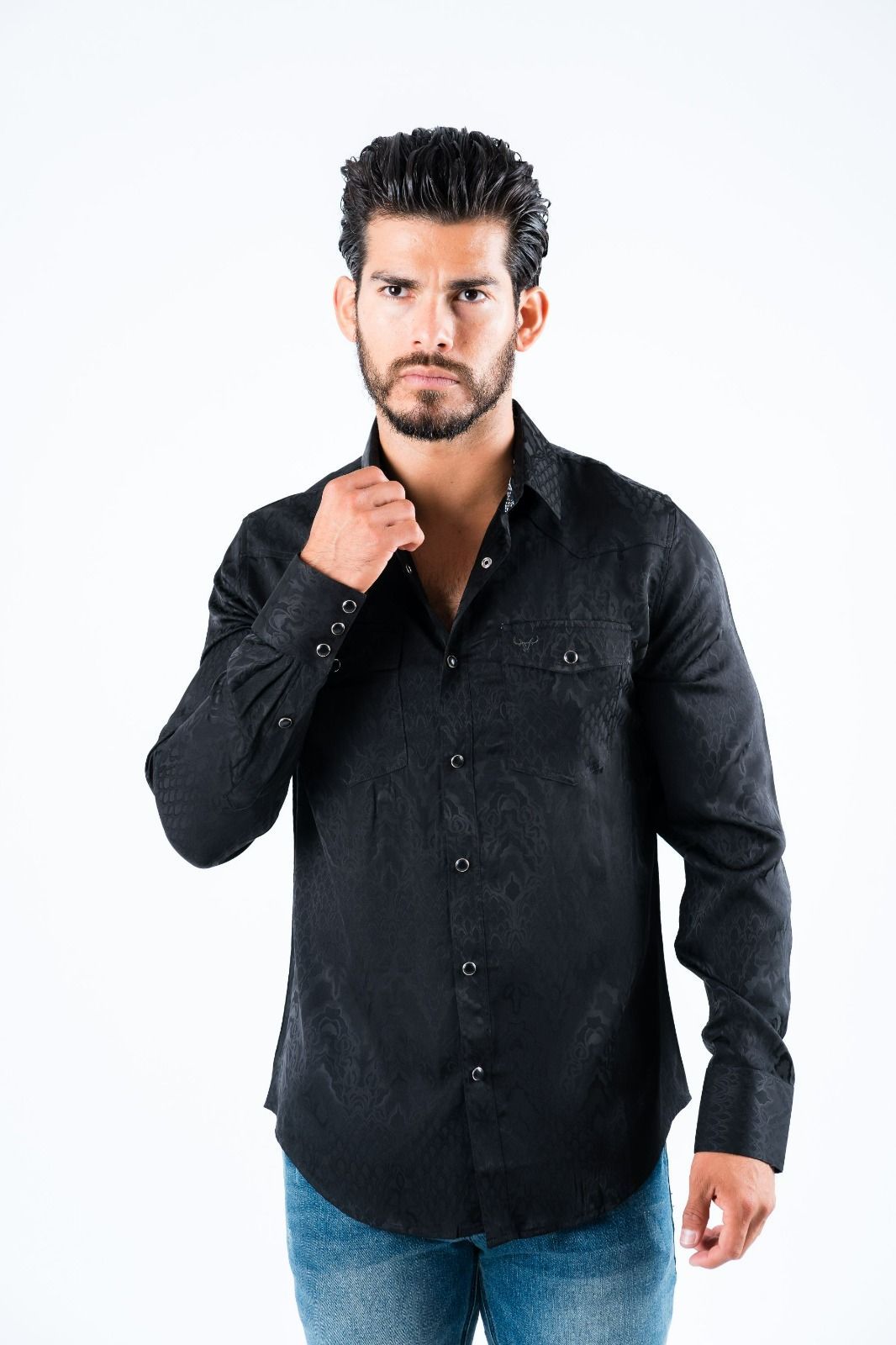 Man in a black shirt posing against a white background, holding his collar.