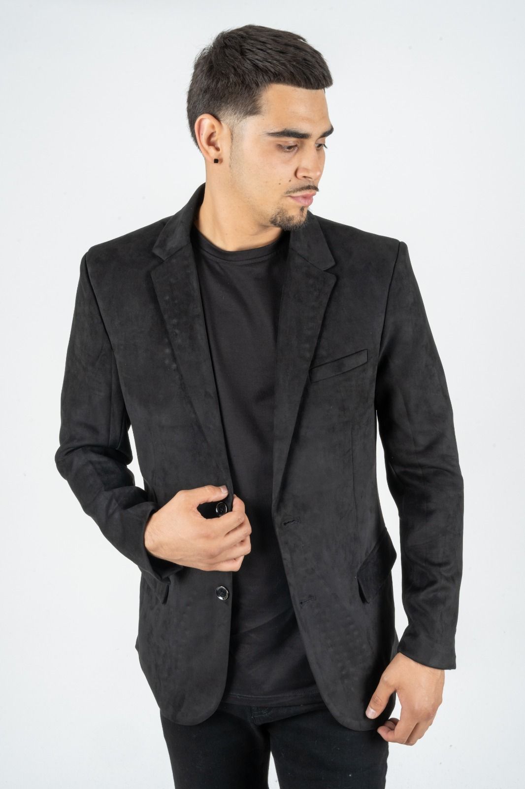 Man in a black blazer and shirt, adjusting his jacket against a white background