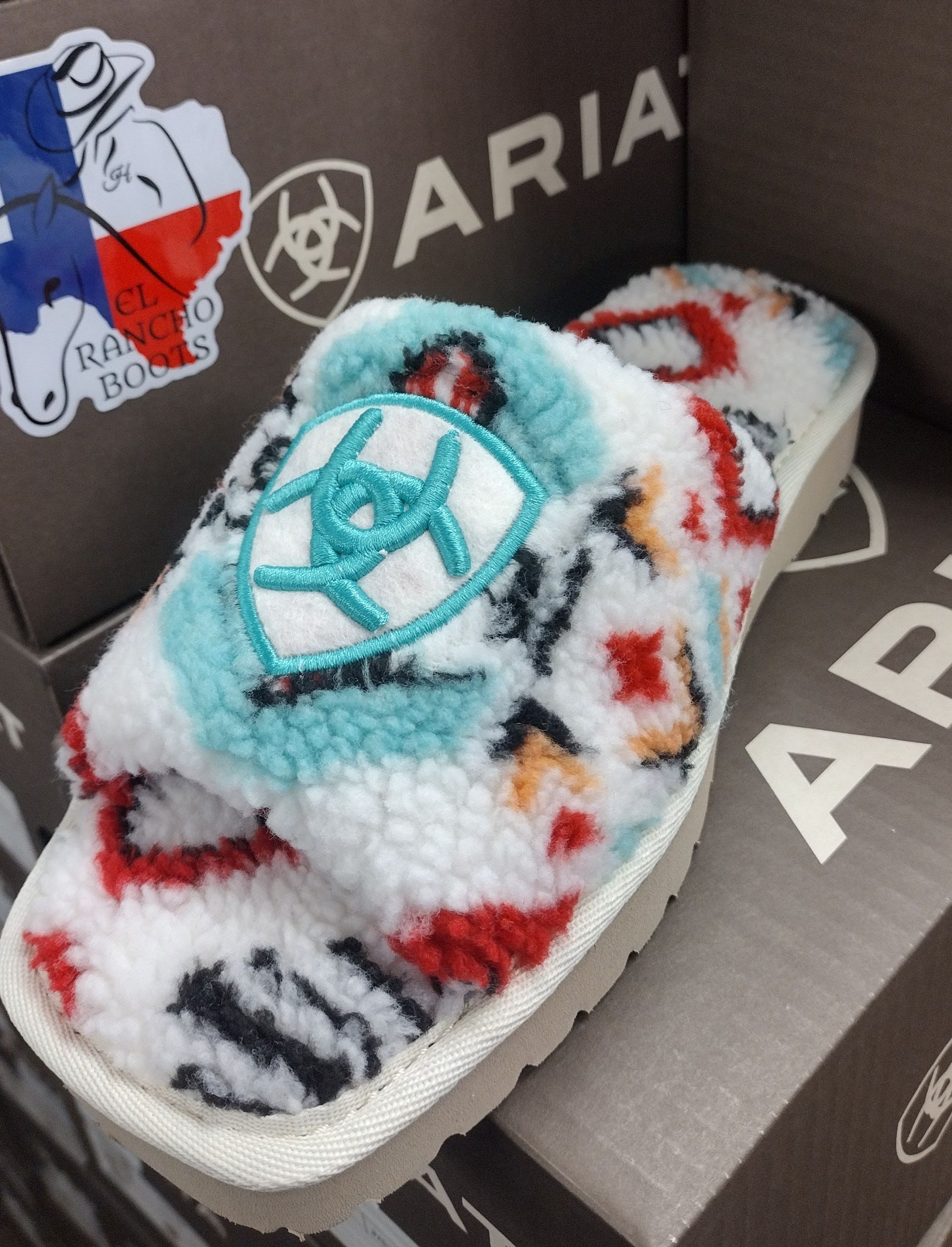 Fluffy white slipper with colorful pattern and turquoise logo on an ARIA shoebox display