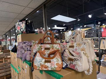 Handbags displayed on stacked boxes inside a retail store, with clothing racks in the background