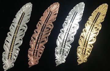 Four ornate leaf-shaped metal bookmarks in silver, copper, silver, and gold on a black background