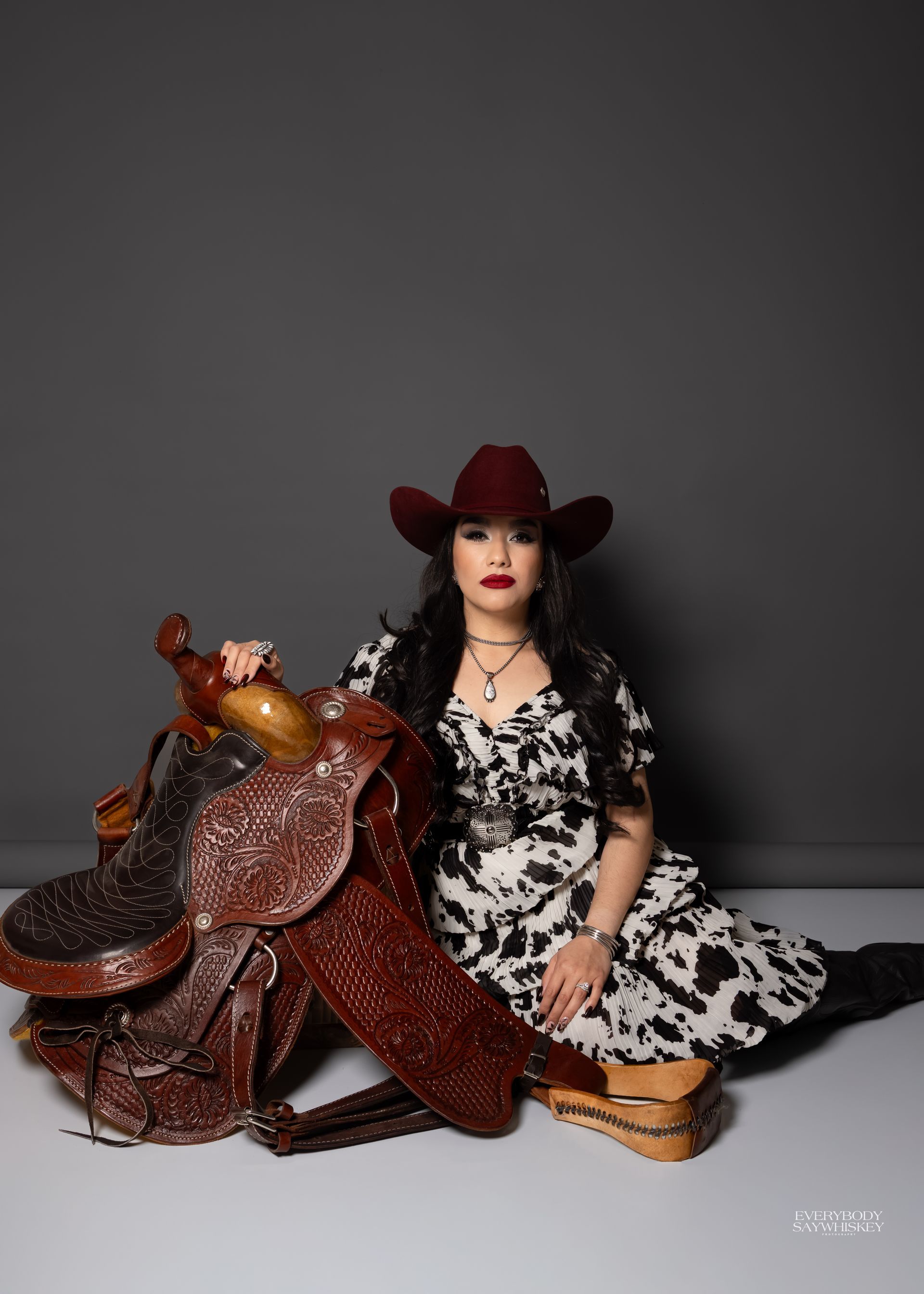 Person in a red hat posing beside a large brown-and-gold decorative horse figure on a gray backdrop