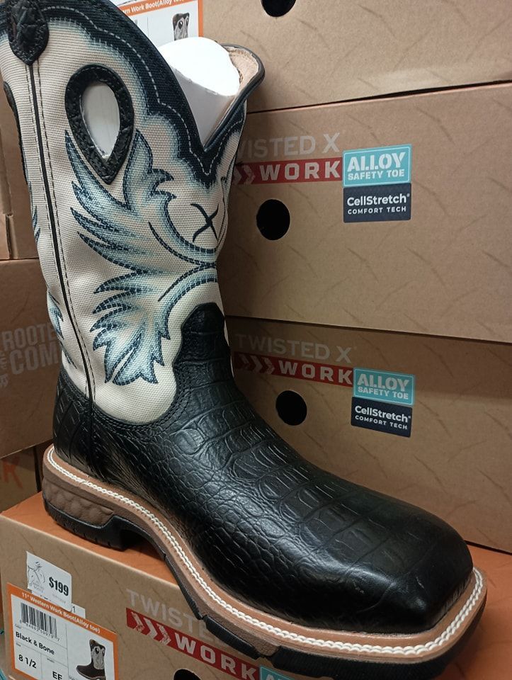 Black cowboy boot with white embroidered shaft displayed on stacked boot boxes.