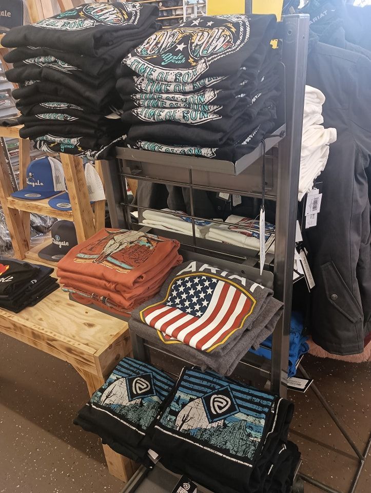 Folded graphic T-shirts stacked on a store rack and table, including black, orange, and striped designs.