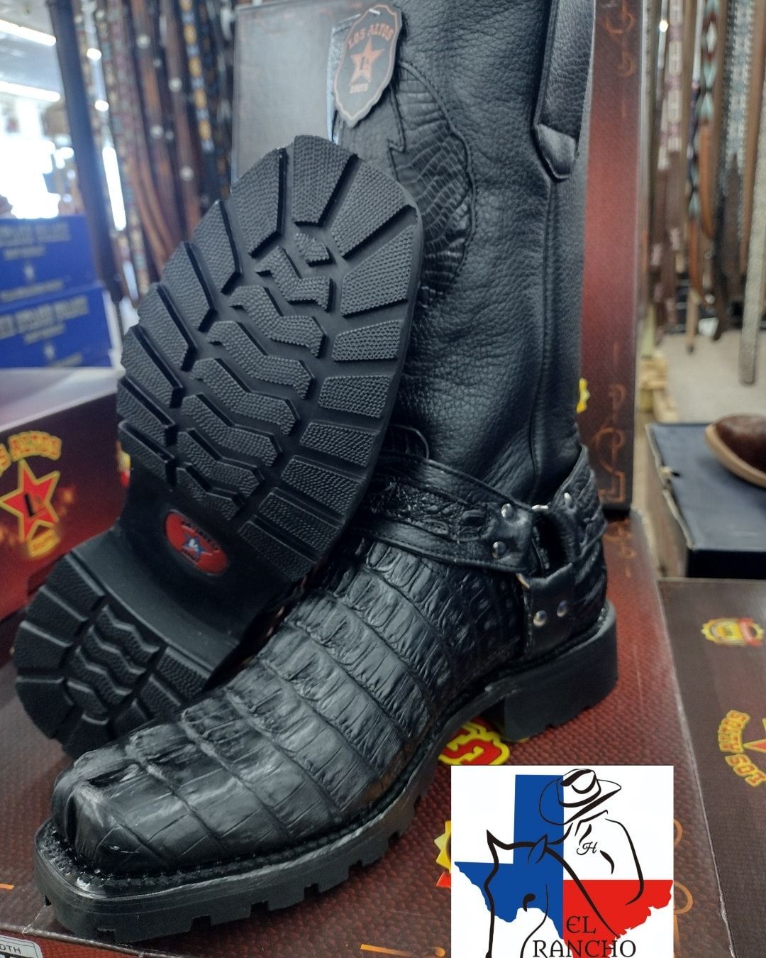 Black leather lace-up boot with thick tread sole, shown from side and bottom on a retail display.