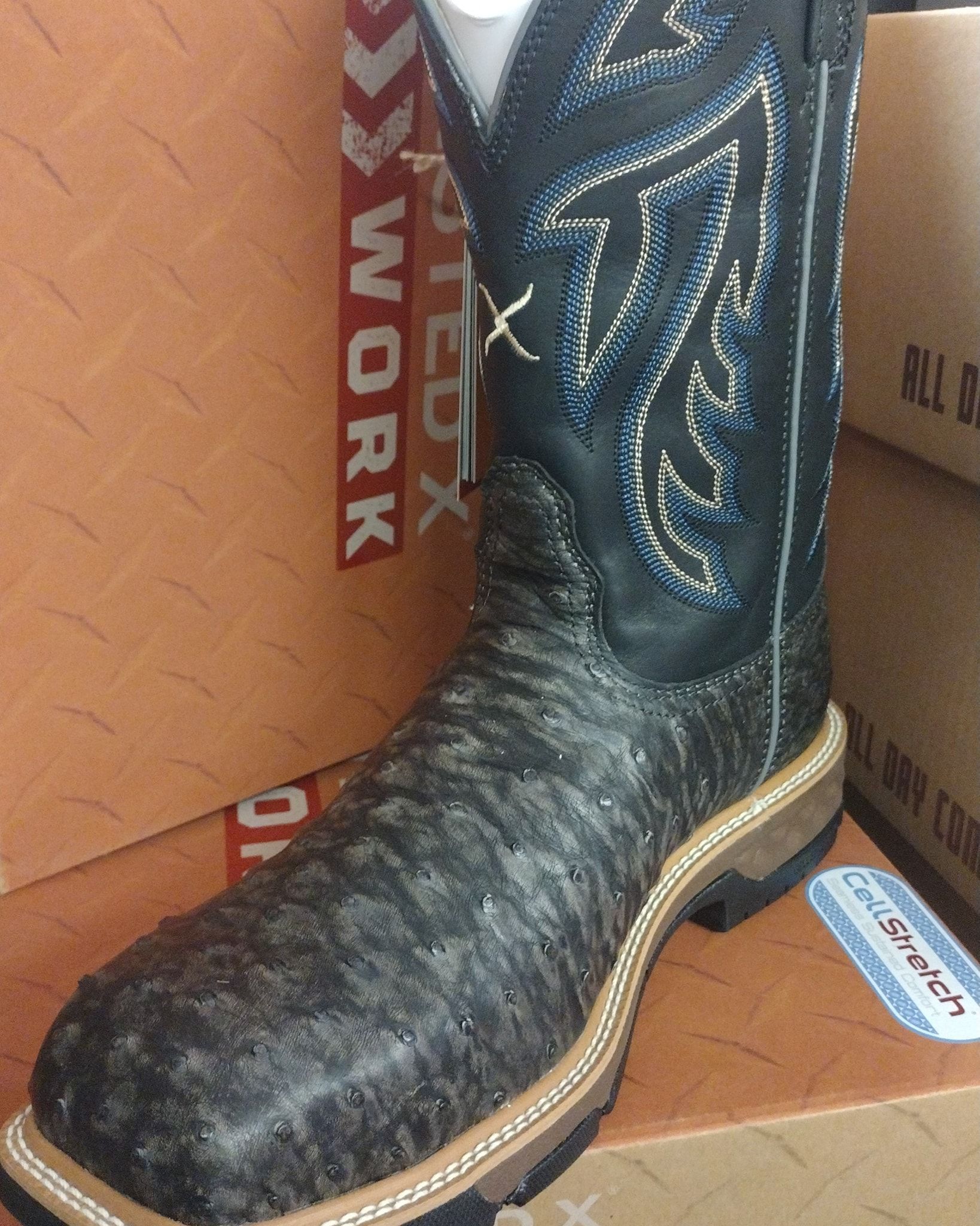 Black cowboy boot with tan sole standing in a cardboard box