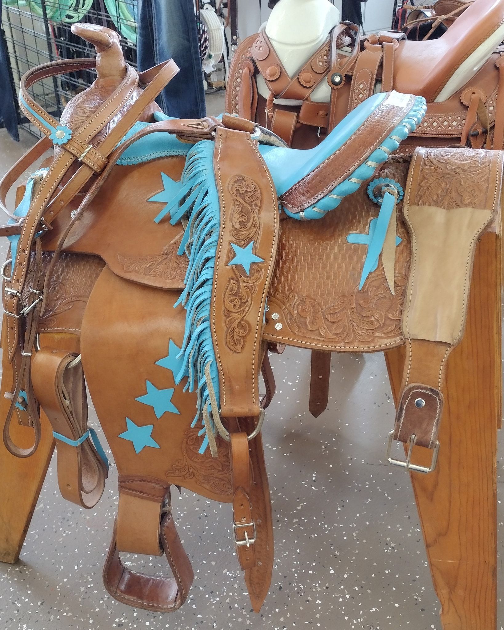 Brown leather saddle with turquoise stars on a horse, shown in a stable setting