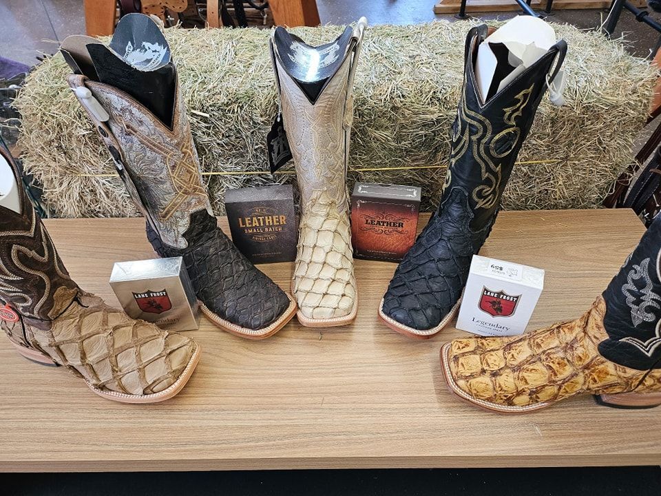 Assorted embroidered cowboy boots on a wooden display shelf with price tags.