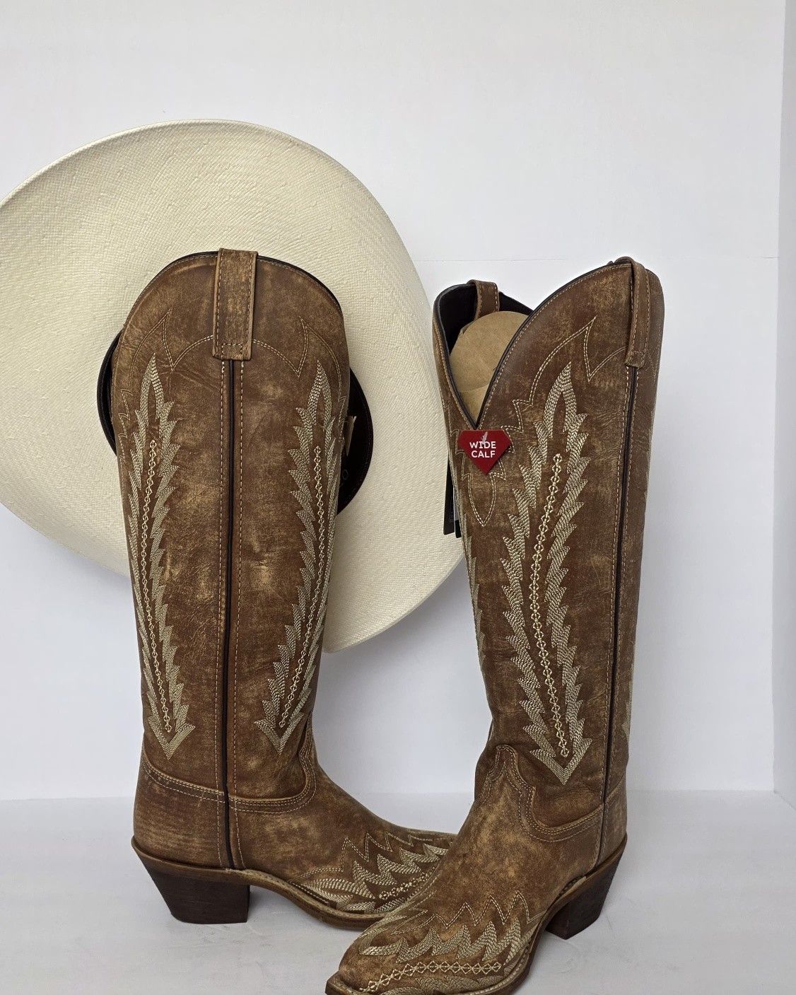 Brown cowboy boots with stitched detailing, displayed in front of a white hat.