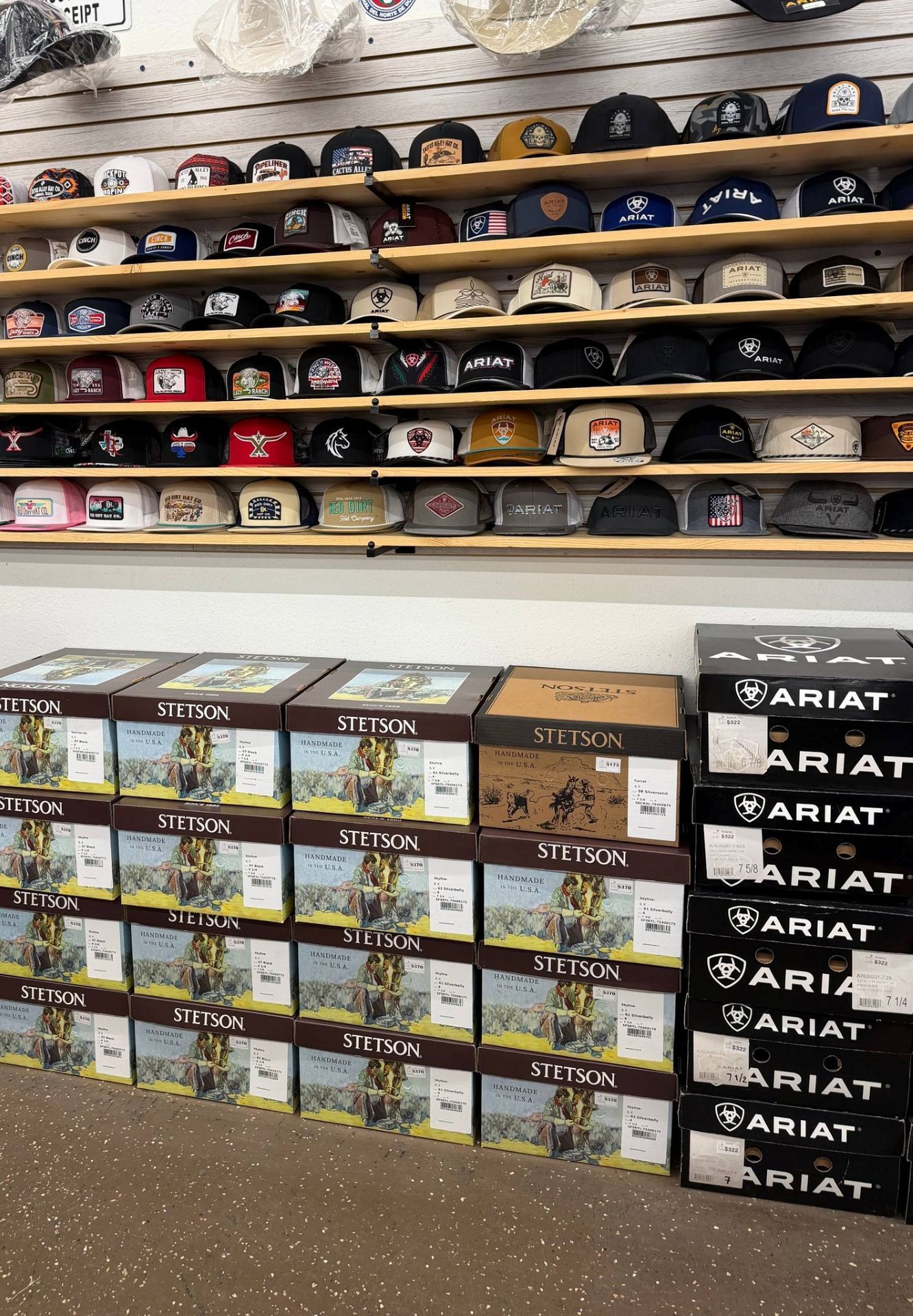 Store shelves lined with many branded hats and Ariat boxes in an indoor retail display
