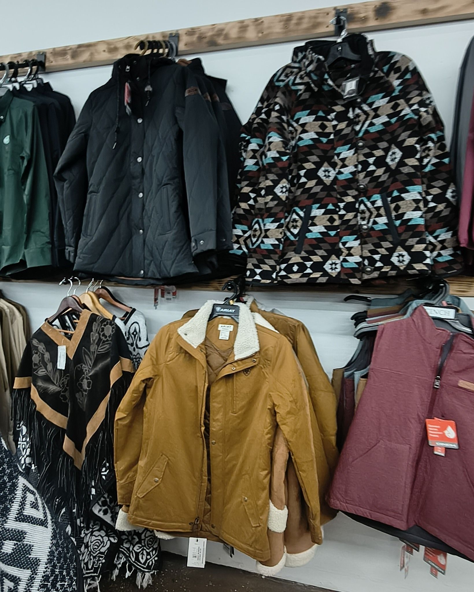 Winter jackets hanging on a shop rack, including black, patterned, tan, and maroon coats.
