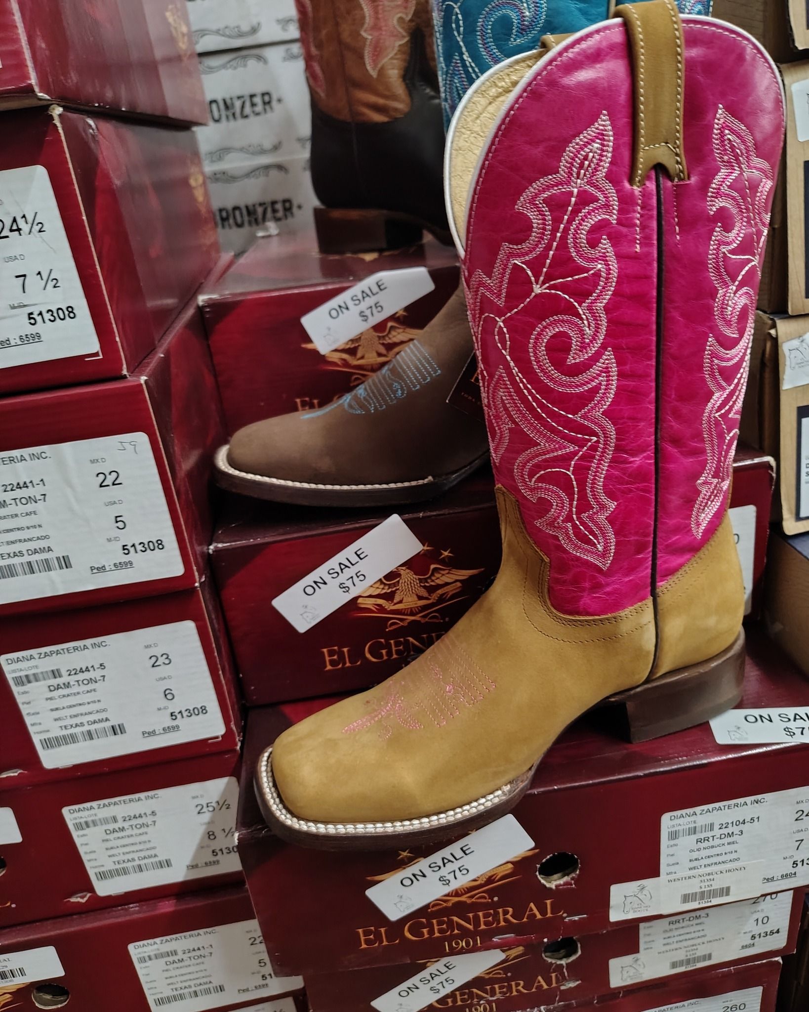Pink-and-tan cowboy boots stacked on red shoe boxes in a store display