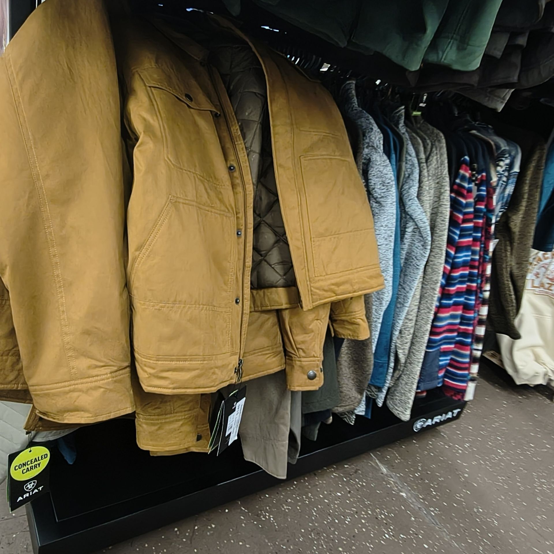 Rack of winter coats and jackets in mustard, gray, and striped patterns hanging in a store aisle