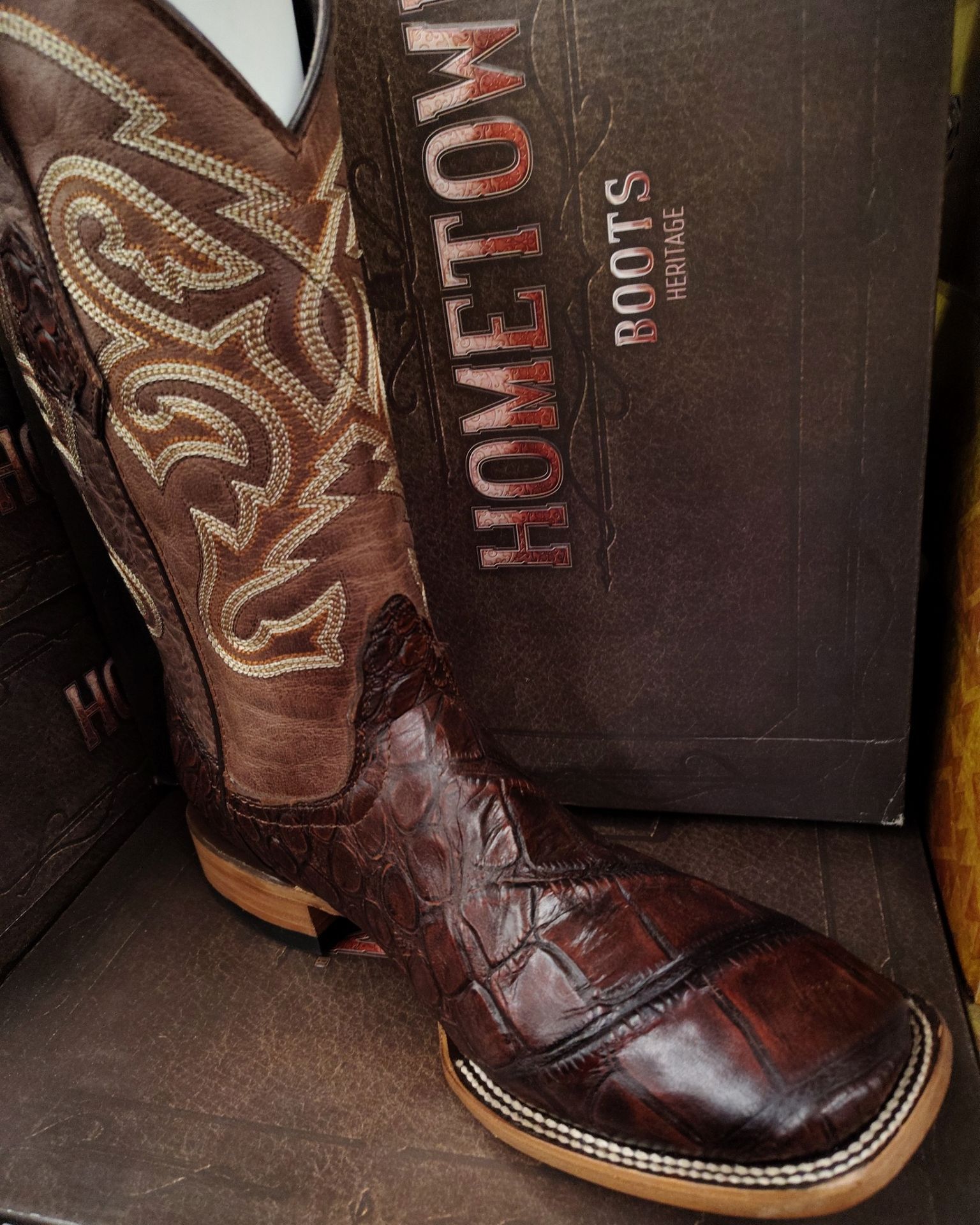 Brown leather cowboy boots with decorative stitching beside a HOMETOWN boots box.