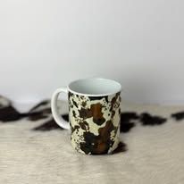 White mug with a brown and black floral pattern on a soft, light-colored surface against a plain wall.