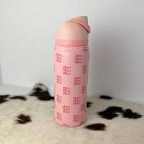 Pink travel bottle with a flip-top cap standing on a spotted blanket