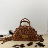 Brown floral-embossed handbag with fringe handles on a fur rug against a white background