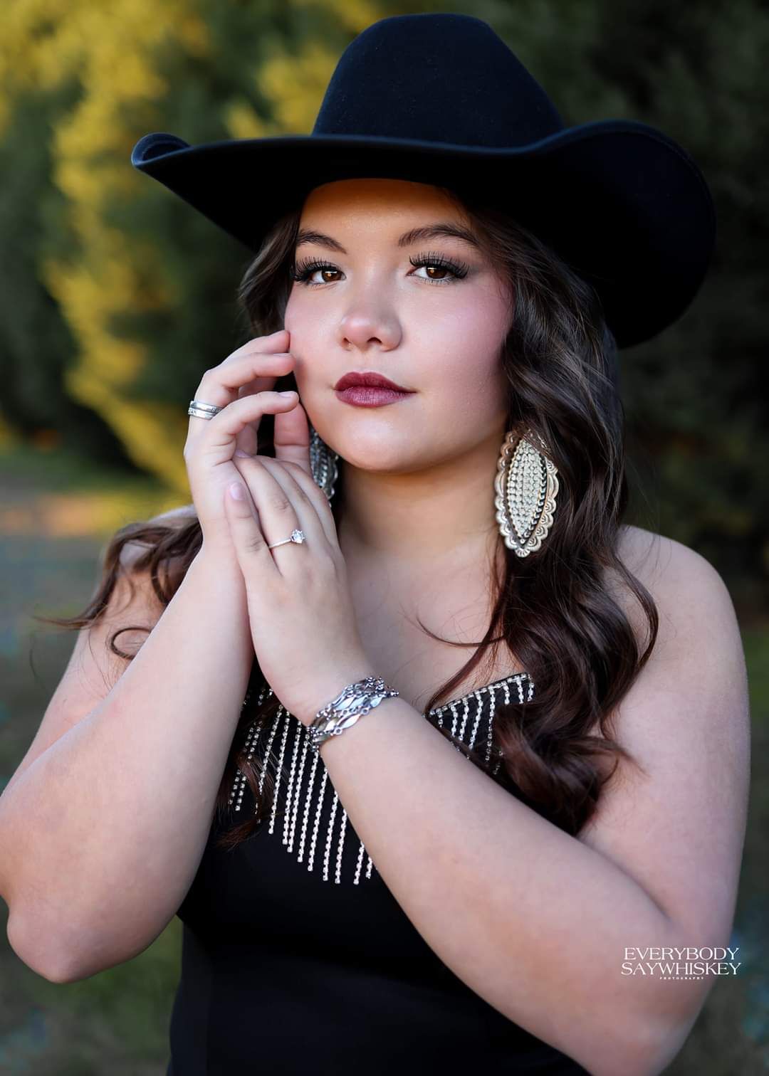 Woman in a black cowboy hat and beaded top posing outdoors with a calm expression