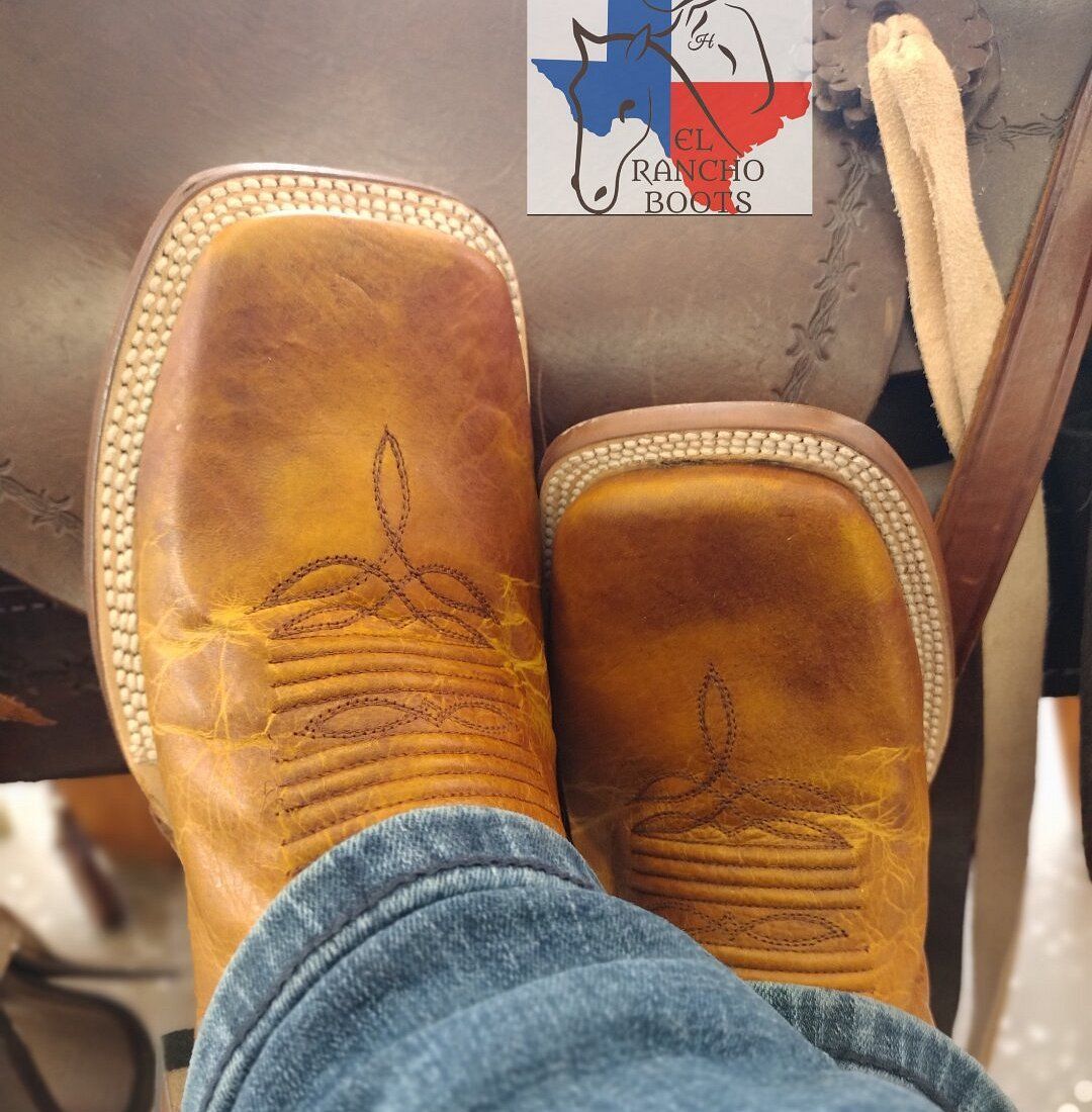 Brown cowboy boots with jeans, resting on a car floor near a small logo sticker.