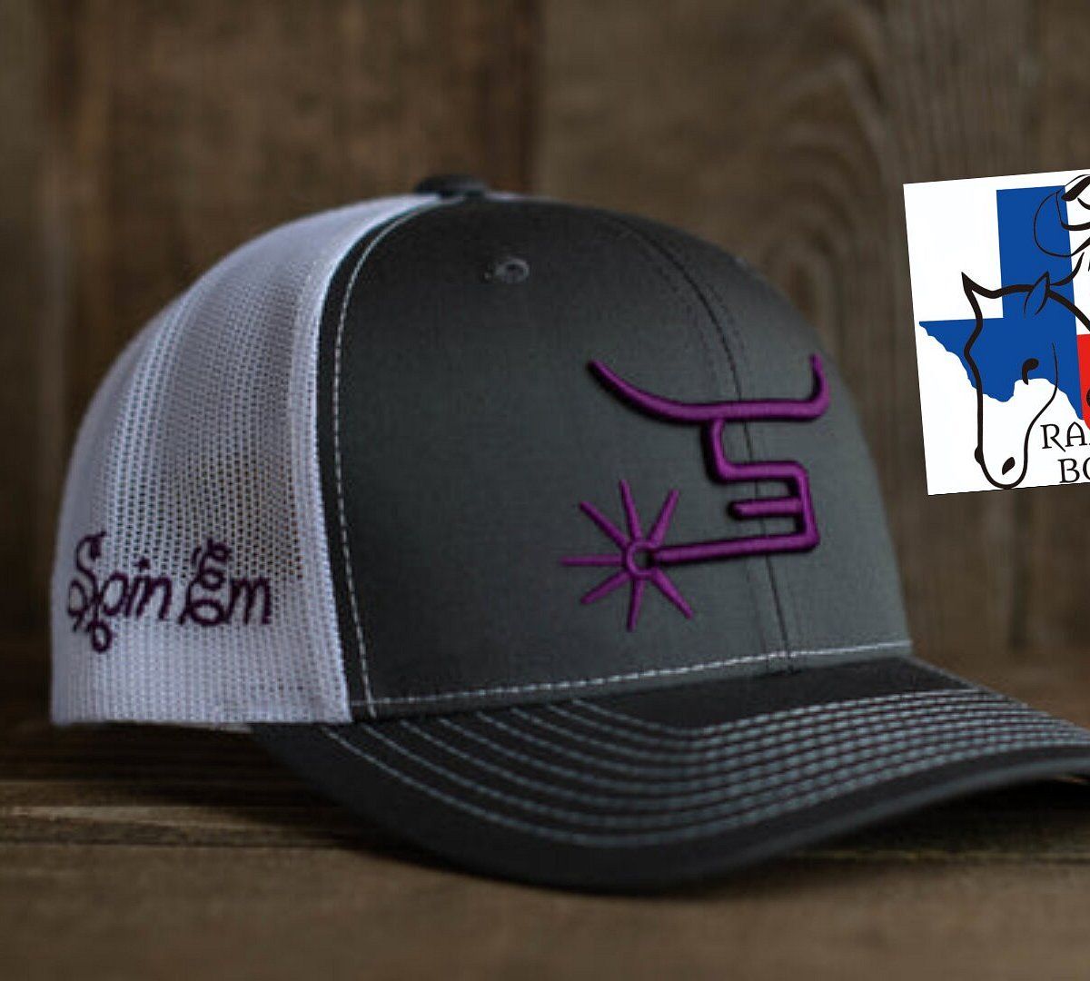 Gray and black mesh trucker cap with purple logo on the front, resting on a wooden surface.