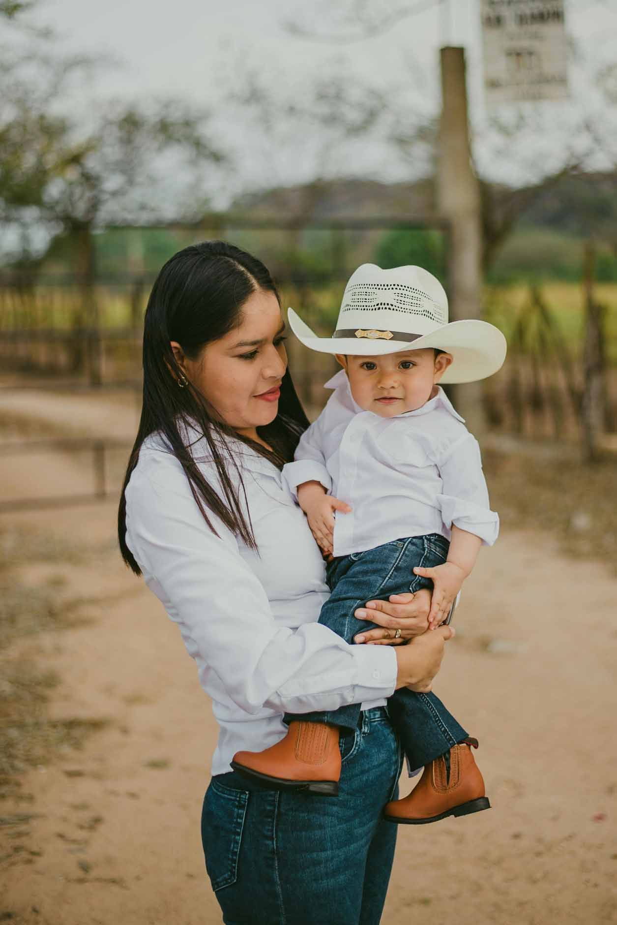 Woman holding a child in a white cowboy hat on a dirt path outdoors