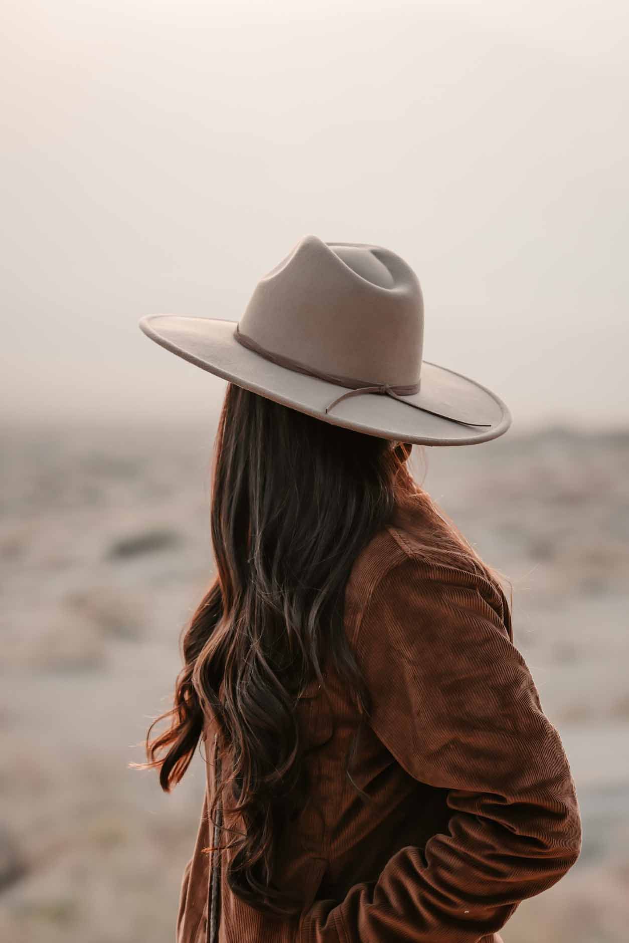 Person in a tan hat and brown jacket, seen from behind in a misty desert landscape.
