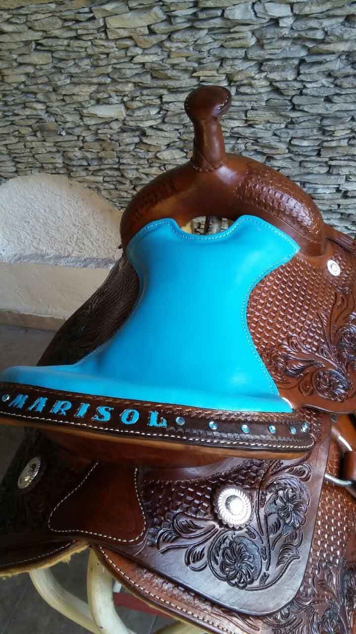 Brown leather saddle with bright turquoise seat and decorative floral tooling on stone surface