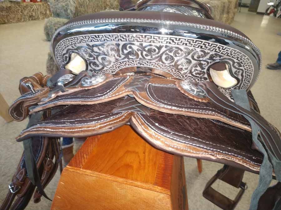 Close-up of a brown leather western saddle with silver engraved detail and horn seat