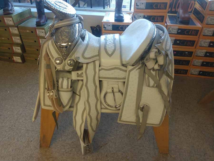 White ceremonial horse armor displayed on a wooden stand in a shop, with silver and gold detailing.