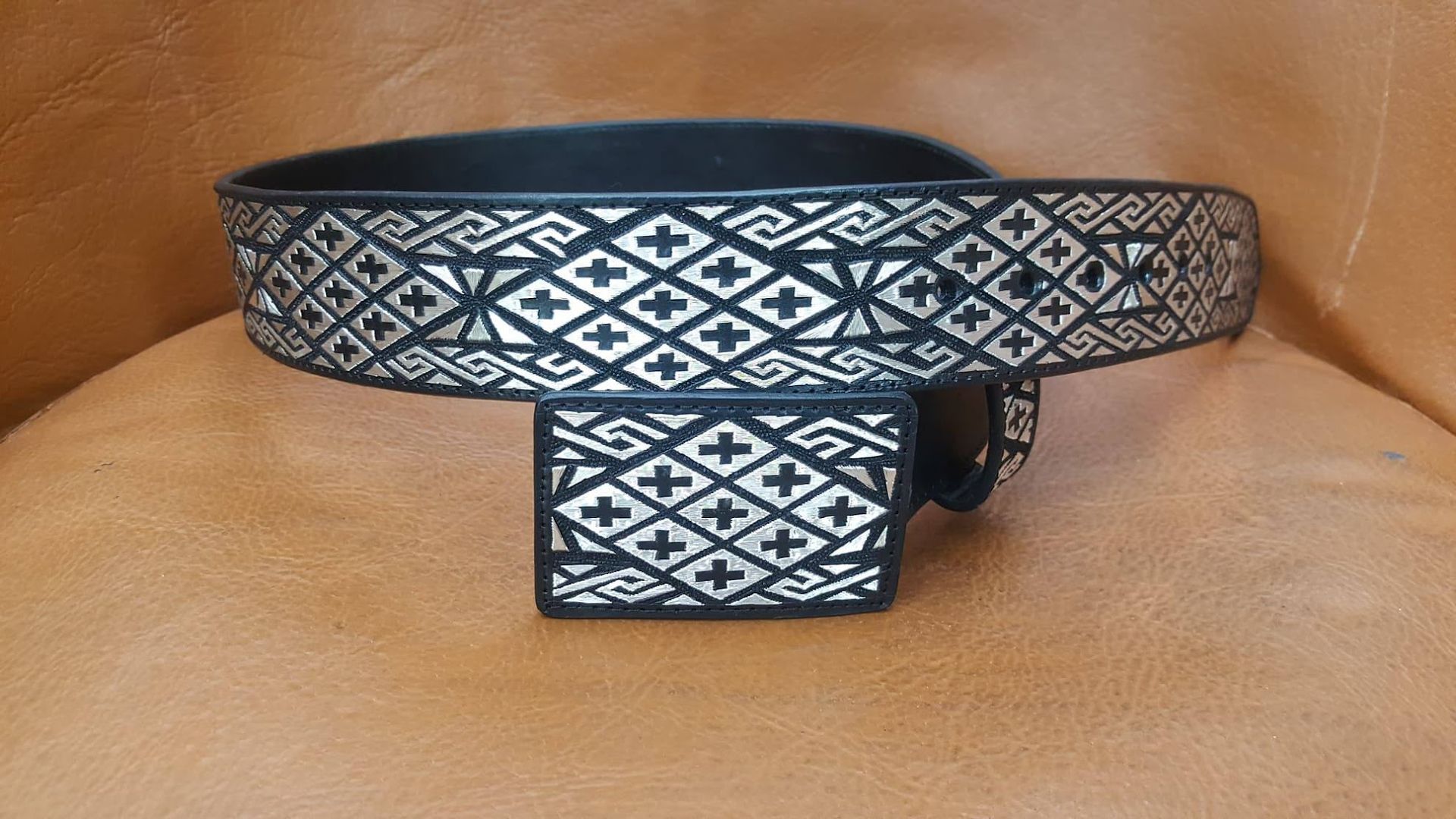 Patterned black-and-white belt and matching buckle on a tan leather chair