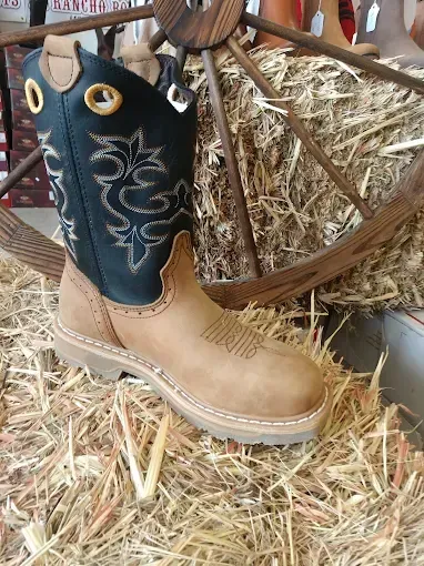 Tan cowboy boot with black shaft leaning on straw in a rustic setting