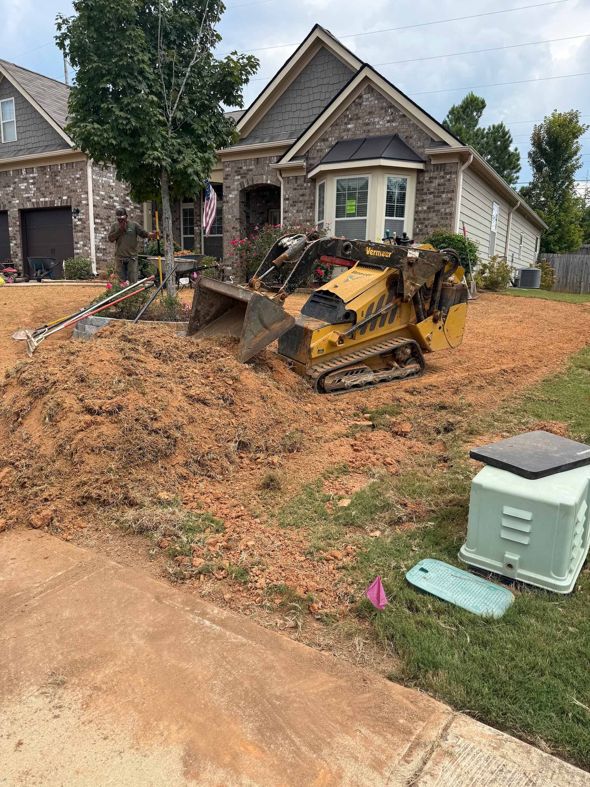 A yellow skid steer tractor is in a yard near a house, moving dirt.