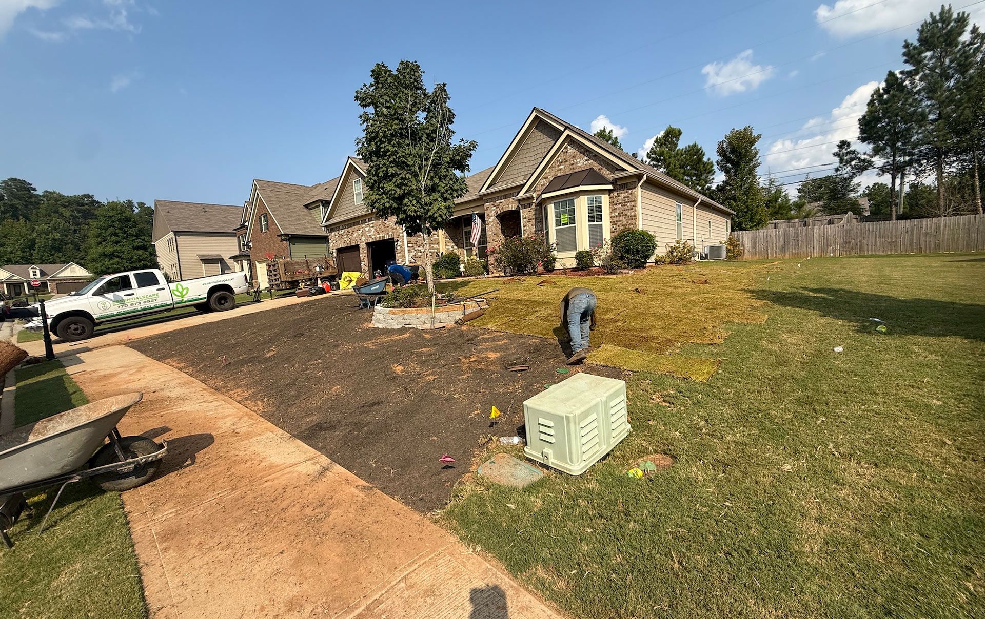 Residential house with landscaping in progress. Dark soil, green grass, and work truck on a sunny day.