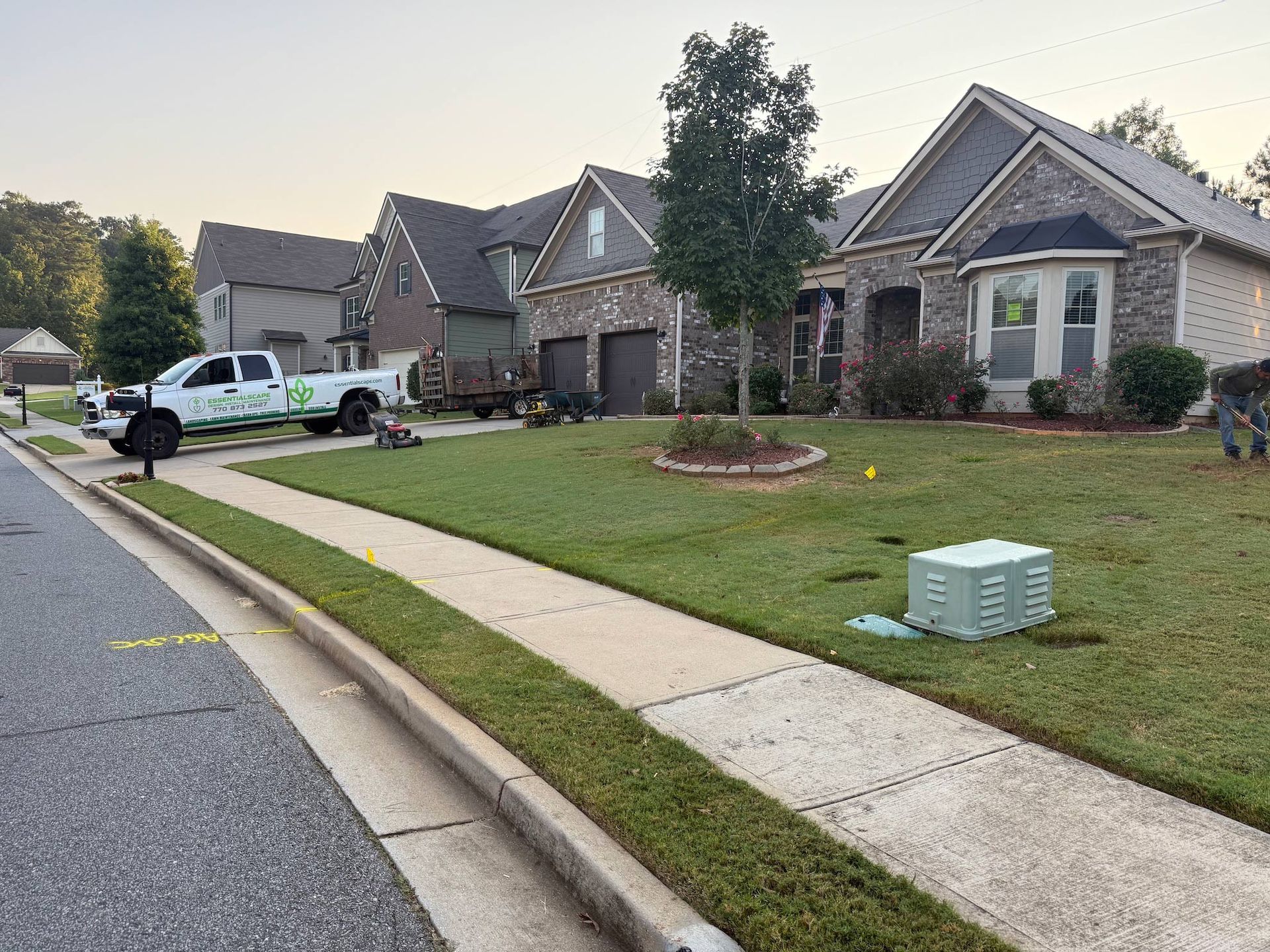 A green lawn being landscaped by a white truck in front of suburban houses on a sunny day.