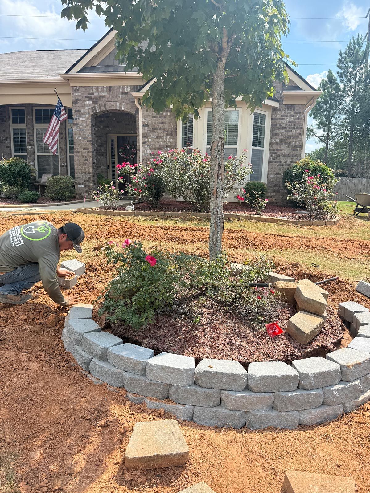 Man building a stone border around a tree in front of a house.