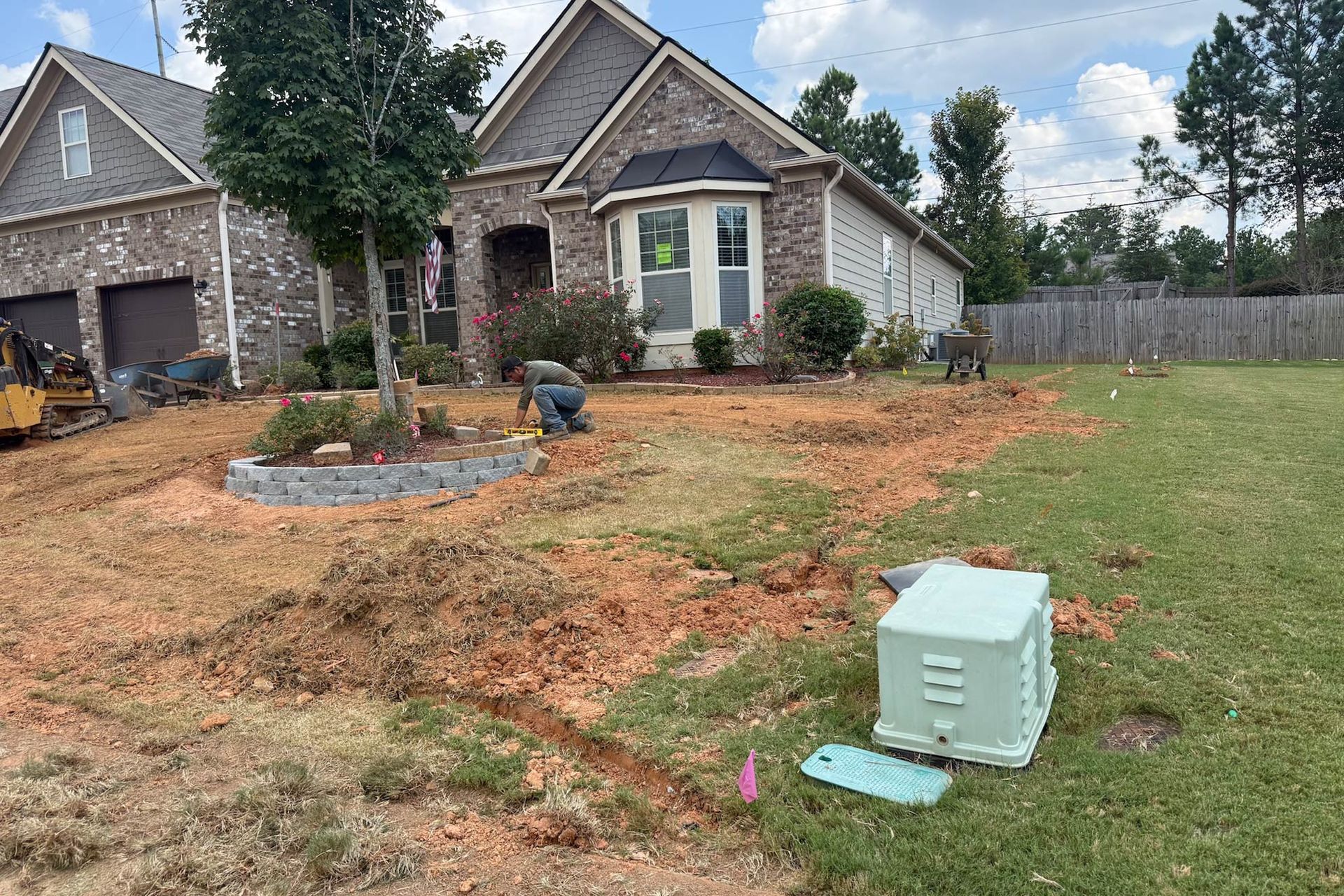 Residential front yard under construction; workers, dirt, house, brick, and grass.