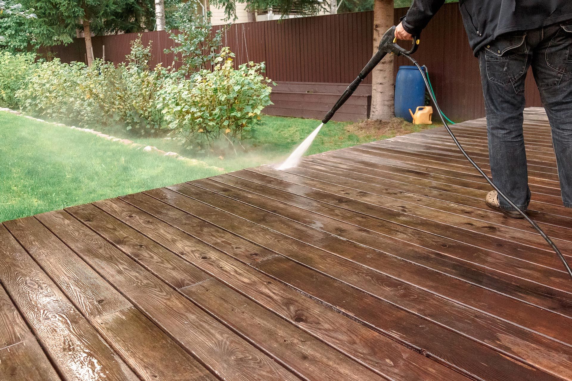 Person pressure washing a wooden deck outdoors.