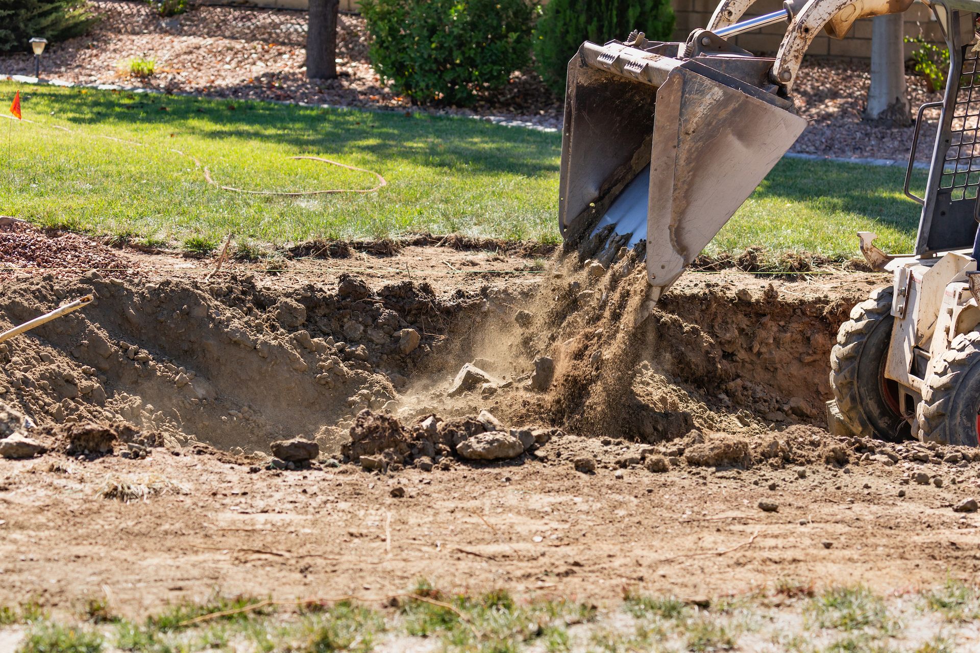 Bobcat excavator dumping dirt into a trench on a grassy lawn.