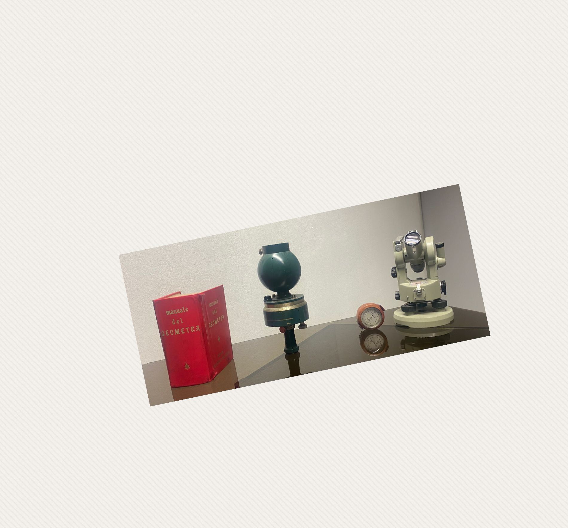 Un libro rosso, un vaso blu e una statuetta bianca sono esposti su uno scaffale inclinato contro una parete beige.