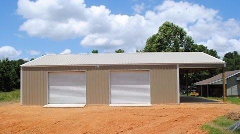 Single-story beige metal building with two roll-up doors on a dirt lot under a cloudy sky